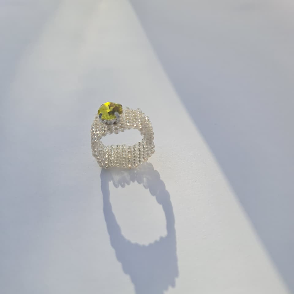 A beaded ring with a textured, openwork design and a small yellow flower-shaped gemstone, displayed on a white surface with a soft shadow.