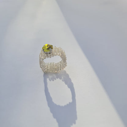 A beaded ring with a textured, openwork design and a small yellow flower-shaped gemstone, displayed on a white surface with a soft shadow.
