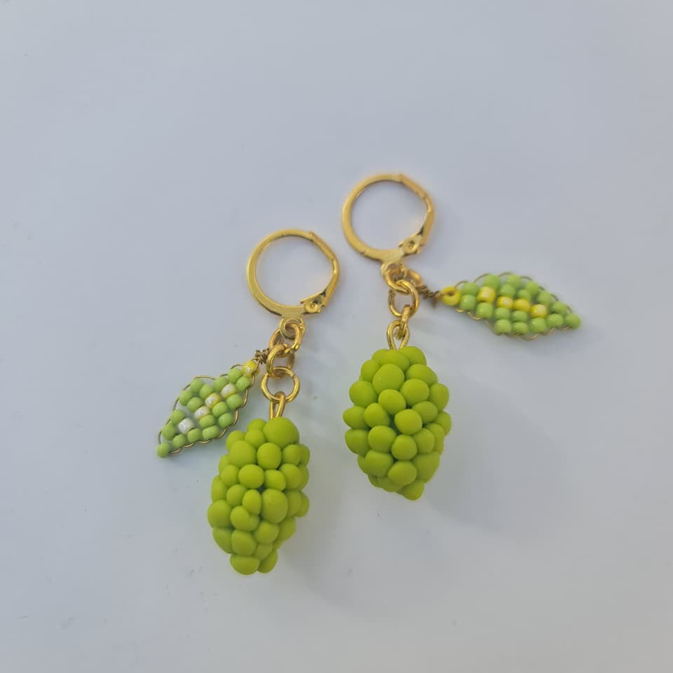 A pair of gold hoop earrings with dangling green grape-shaped charms and small green leaf charms, photographed on a plain light gray background.
