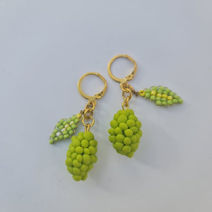 A pair of gold hoop earrings with dangling green grape-shaped charms and small green leaf charms, photographed on a plain light gray background.