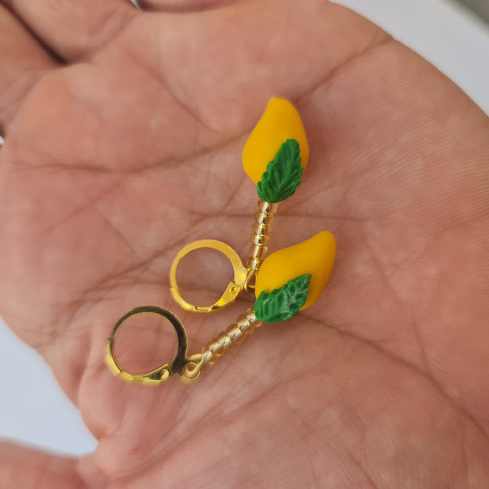 A pair of gold hoop earrings with yellow lemon-shaped charms and green leaf details, resting on an open hand.
