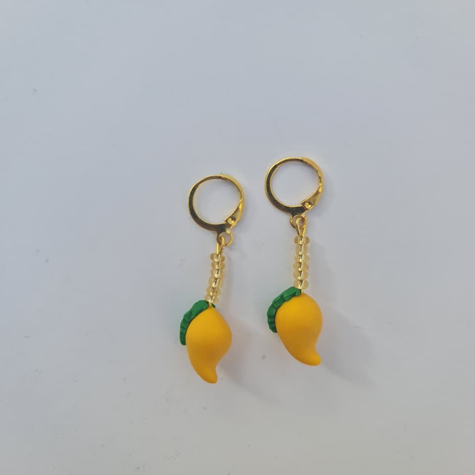 A pair of gold hoop earrings with dangling yellow chili pepper charms and green leaf accents, shown on a plain light gray background.