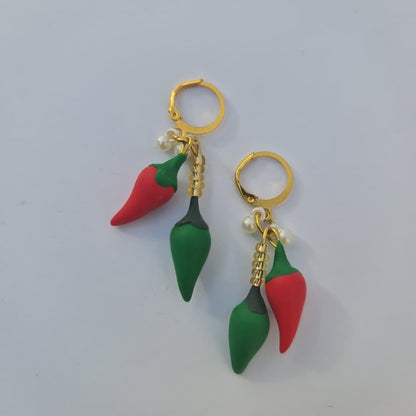 A pair of gold hoop earrings with dangling chili pepper charms, featuring one red and one green pepper charm on each earring, set against a plain light gray background.