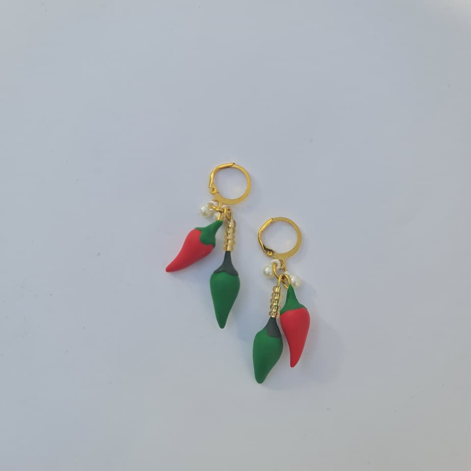 A pair of gold hoop earrings featuring dangling chili pepper charms, with one red pepper and one green pepper hanging from each hoop, displayed on a clean white surface.