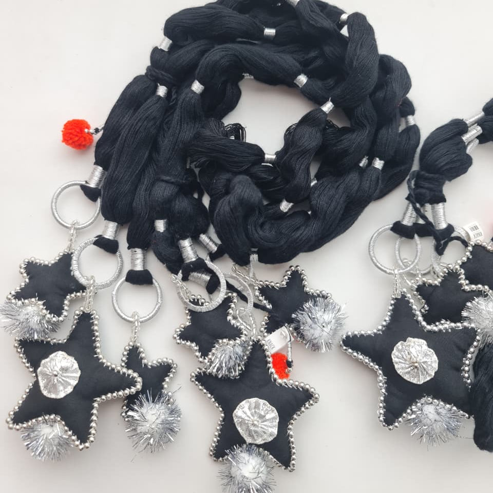 Black fabric star-shaped jewelry charms with silver beaded edges, silver pom-poms, and silver circular center details, shown with black braided cords and metal rings on a plain light background.