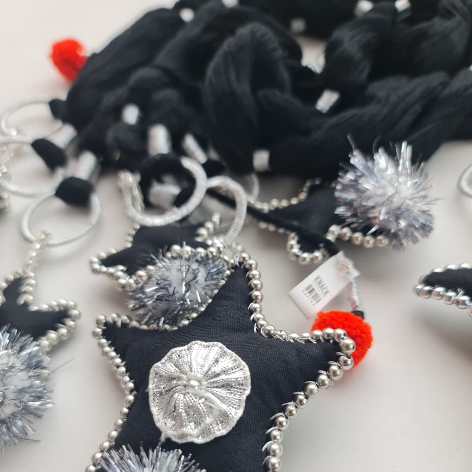 Black felt star-shaped keychain charms with silver beaded edges, silver tinsel pom-poms, and a central silver metallic flower applique, shown on a white background.