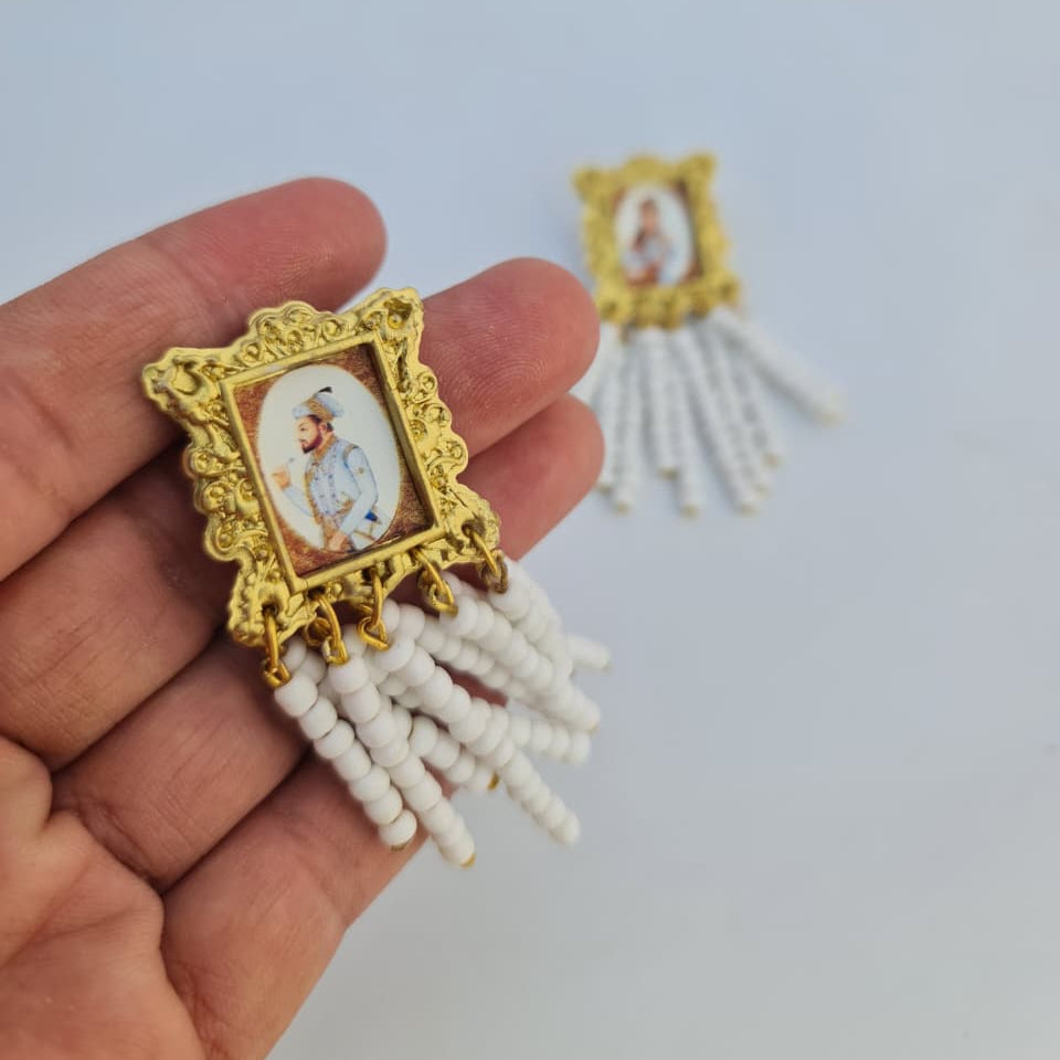 Decorative item with gold frame and white tassels held by a hand on a light background
