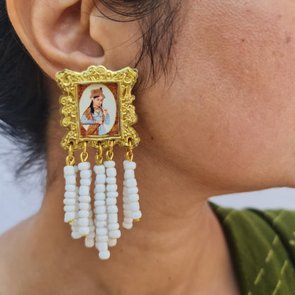 Gold earring with a portrait design and white beads worn by a person.