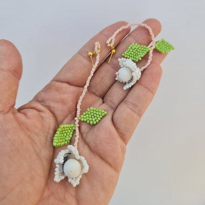Hand holding a delicate necklace with floral and leaf designs on a light background