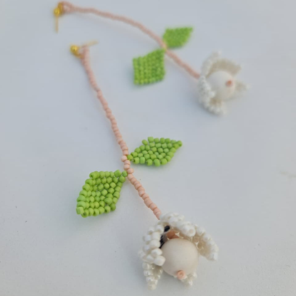 Handmade beaded necklace with green leaves and white beads on a light background