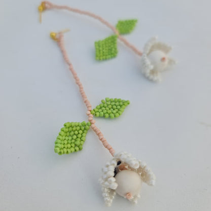 Handmade beaded necklace with green leaves and white beads on a light background