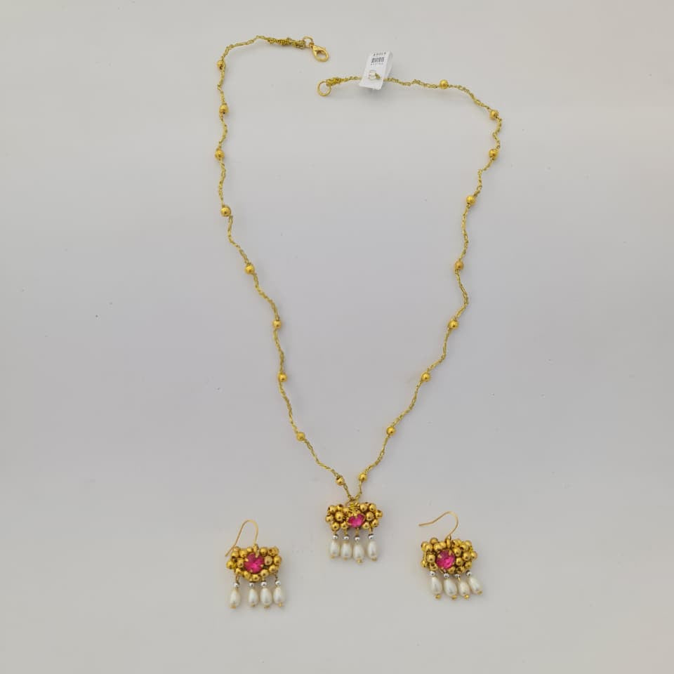 Gold necklace with pink gemstones and pearl drops on a gray background