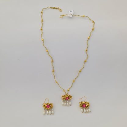 Gold necklace with pink gemstones and pearl drops on a gray background