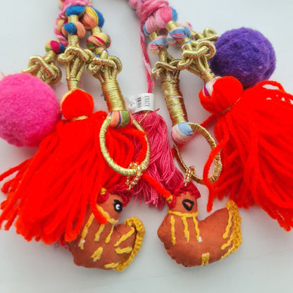 A pair of colorful embroidered keychains featuring red tassels, pink and purple pom-poms, braided multicolor cords, and small rooster-shaped charms, displayed on a white background.