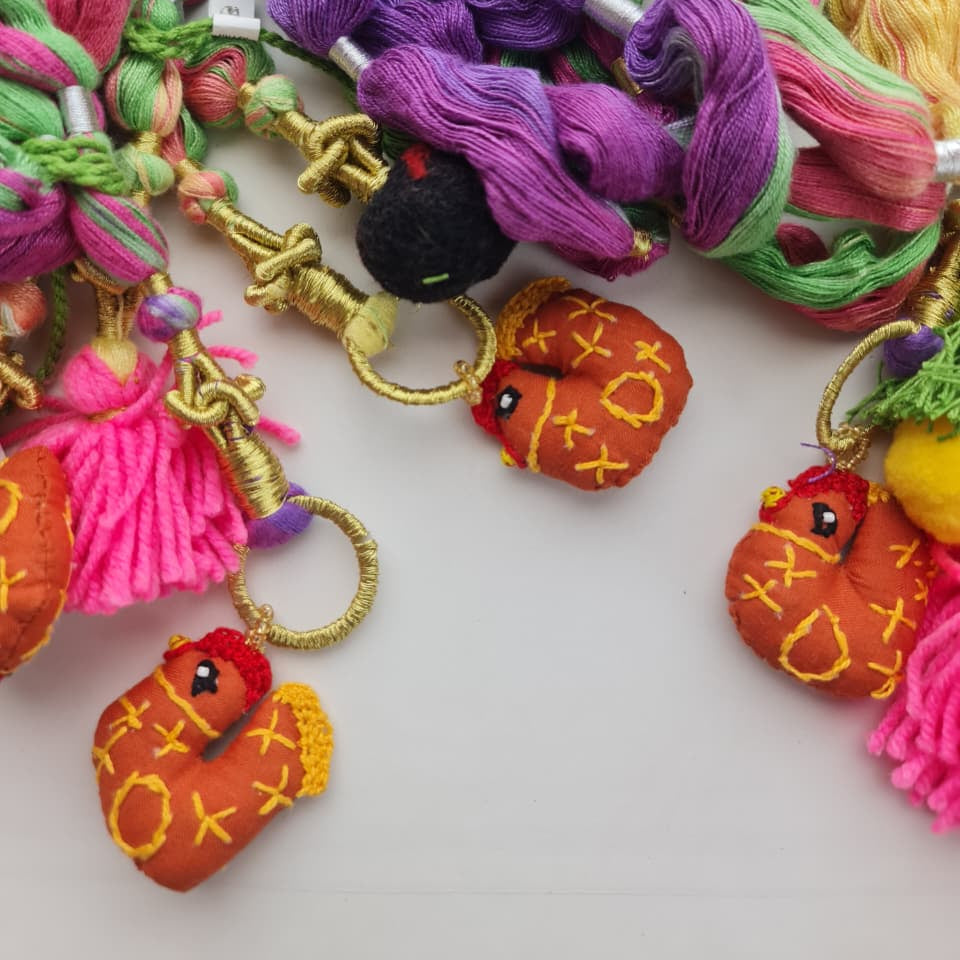 A close-up of colorful embroidery floss skeins in pink, green, purple, and yellow, arranged with small gold-tone rings and tassels on a plain light background.