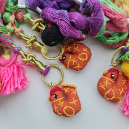A close-up of colorful embroidery floss skeins and matching embroidered bird charms in pink, purple, green, yellow, and orange, arranged on a light background.