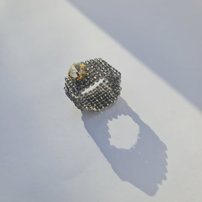 A textured silver ring with a small clear gemstone, resting on a white surface with a sharp shadow cast by direct sunlight.