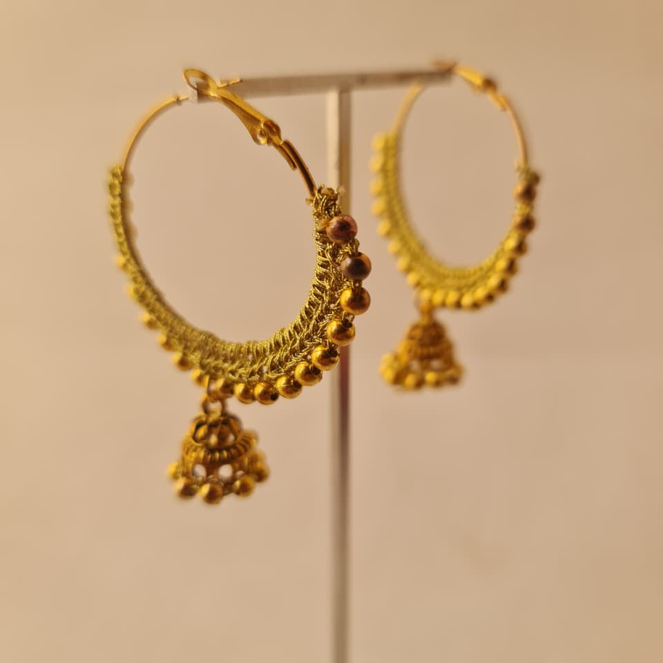 A pair of gold-toned traditional hoop earrings with dangling beaded jhumka-style charms, displayed on a clear stand against a plain beige background.