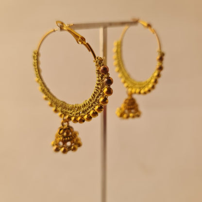 A pair of gold-toned traditional hoop earrings with dangling beaded jhumka-style charms, displayed on a clear stand against a plain beige background.