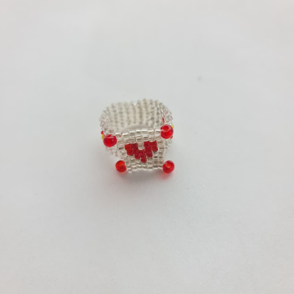 A small handmade beaded box charm or miniature accessory made of silver seed beads with red bead accents, shown on a plain white background.