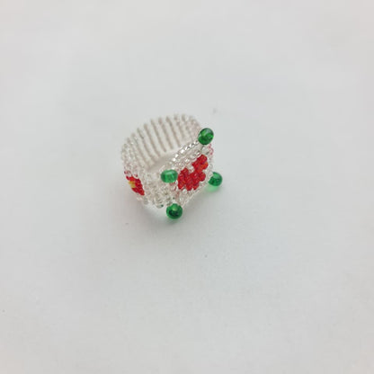 A handmade beaded ring featuring a white textured band decorated with red and green beads, photographed on a plain white background.