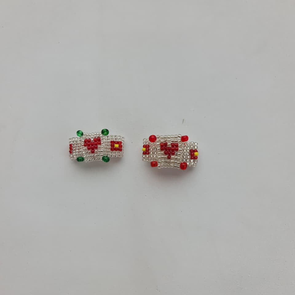 A pair of small rectangular beaded jewelry pieces, likely earrings or charms, featuring a white beaded border, a red heart motif, and small green and yellow accents, displayed on a plain light gray background.