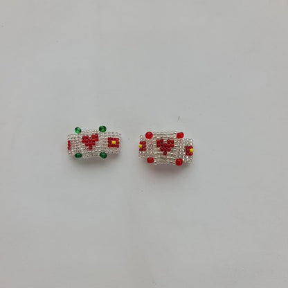 A pair of small rectangular beaded jewelry pieces, likely earrings or charms, featuring a white beaded border, a red heart motif, and small green and yellow accents, displayed on a plain light gray background.