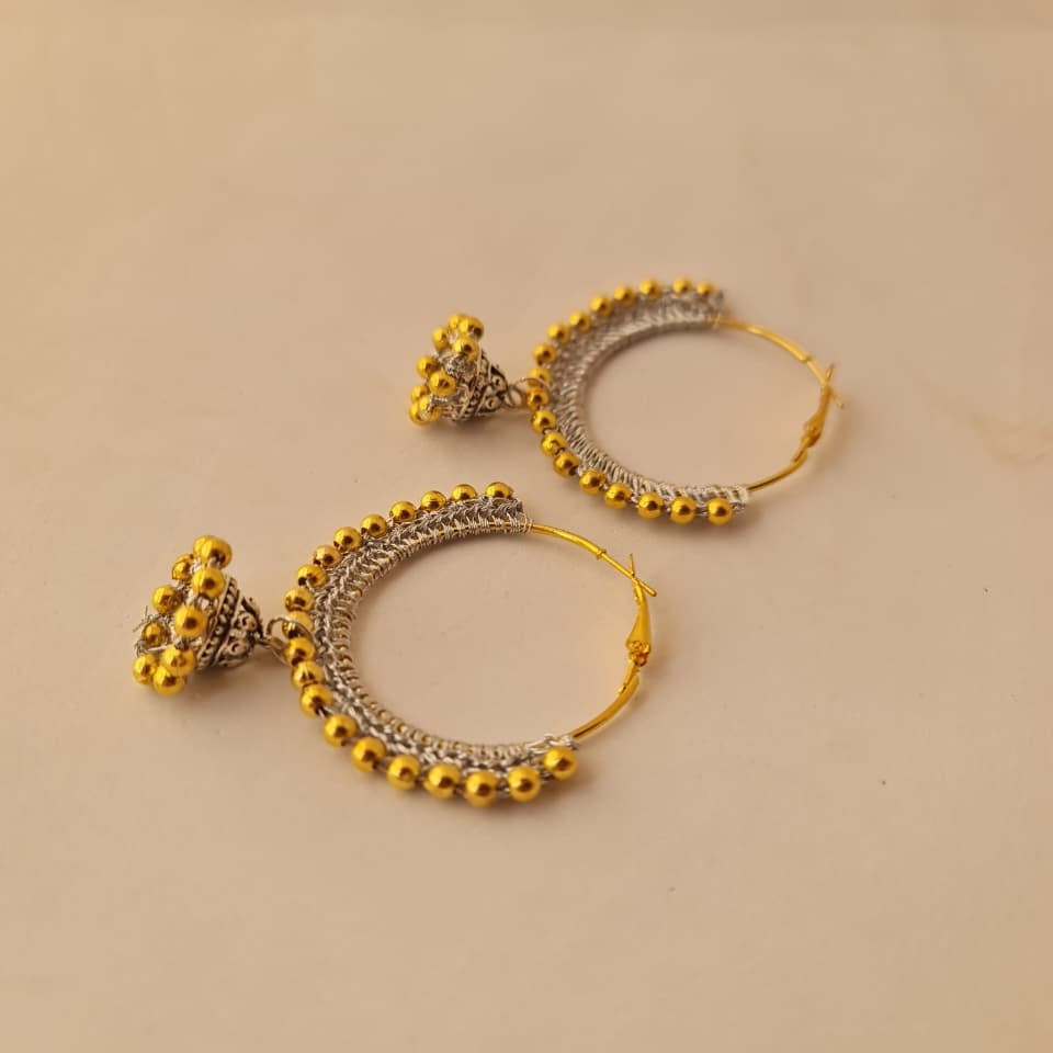 A pair of gold and silver-toned traditional hoop earrings with dangling beaded tassels, displayed on a plain beige background.