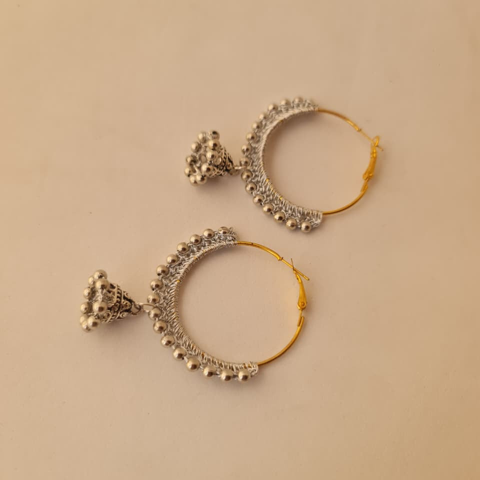 A pair of gold and silver hoop earrings with intricate silver filigree and bead details, displayed on a solid beige background.