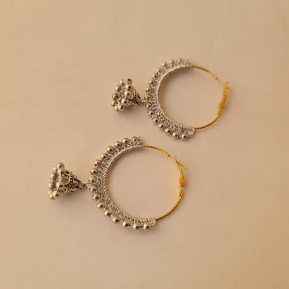 A pair of gold and silver hoop earrings with intricate silver filigree and bead details, displayed on a solid beige background.