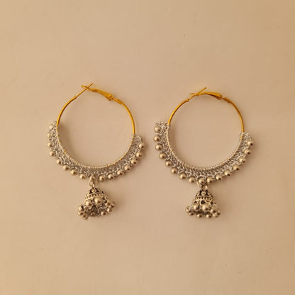 A pair of gold and silver-toned hoop earrings with intricate beadwork and dangling bell-shaped charms, displayed on a plain beige background.
