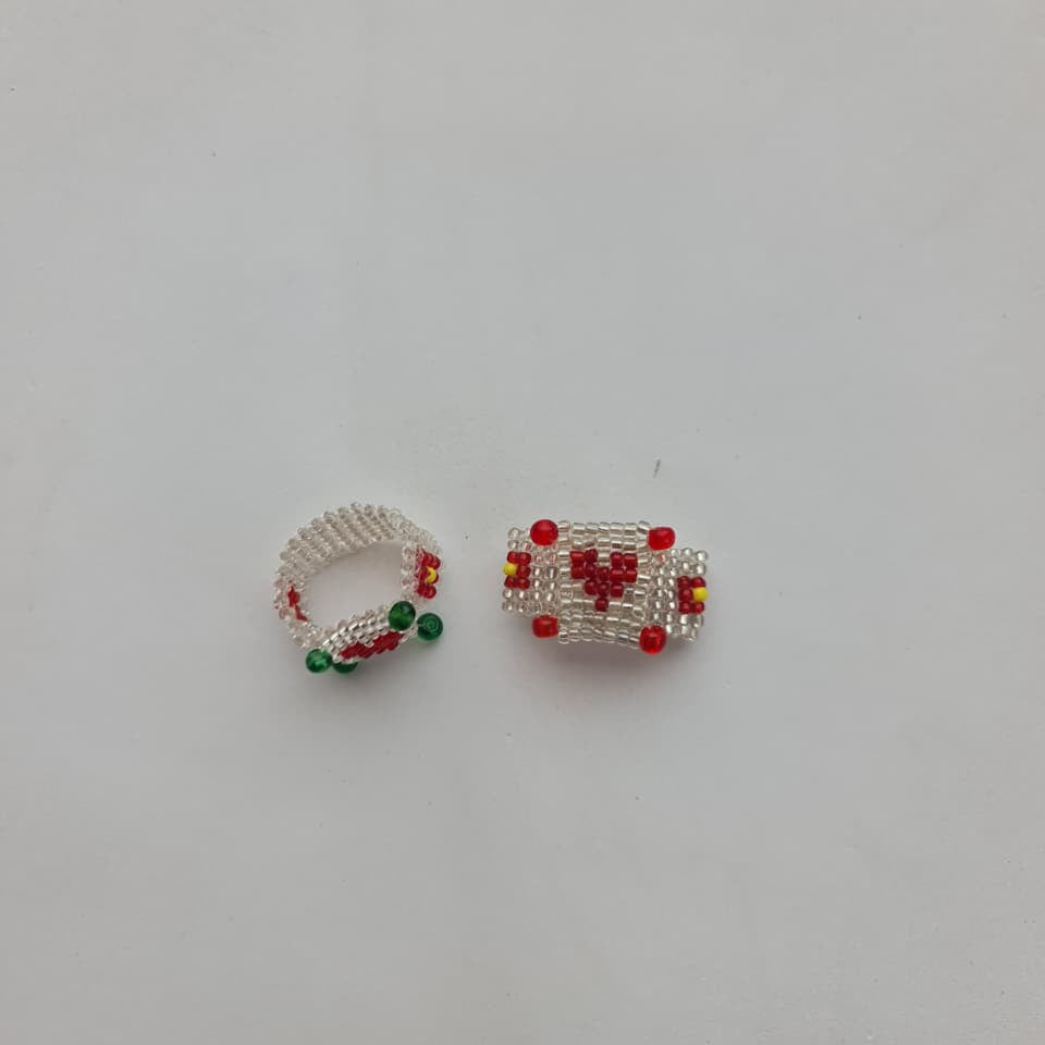 Two small handmade beaded jewelry pieces, one a ring and one a rectangular charm or connector, featuring white seed beads with red and green accents, on a plain white background.