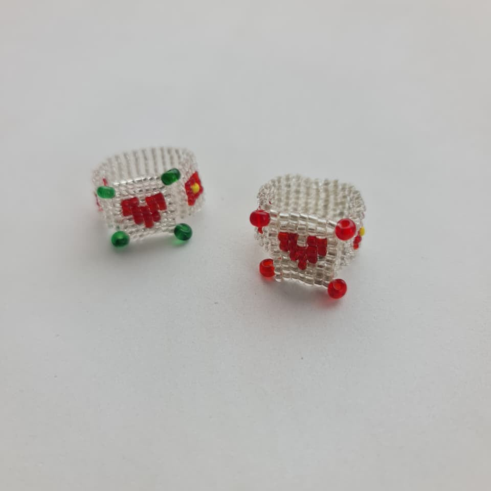 Two small silver mesh jewelry pieces with red and green bead details, photographed on a plain light background.